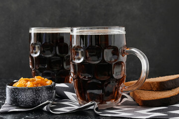 Mugs of fresh kvass and raisins on dark background