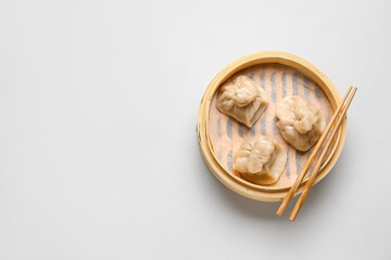 Bamboo steamer with tasty dumplings and chopsticks on light background