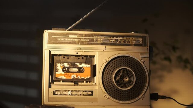 Old vintage broken silver cassette player stands on table and plays audio cassette with MUSIC inscription on label. Slow dolly footage of retro player.