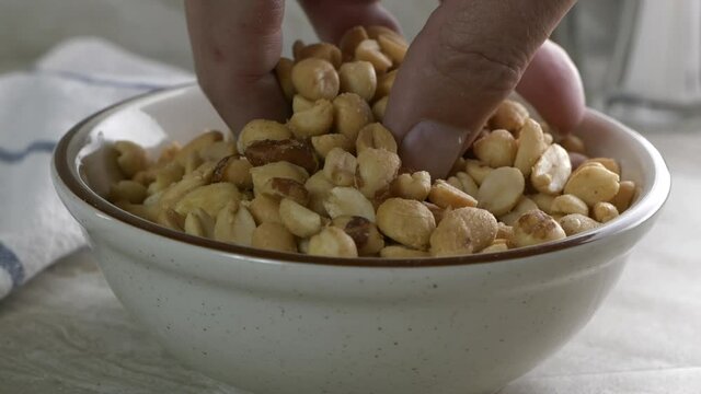 Fingers taking peanuts out of a bowl in super slow motion