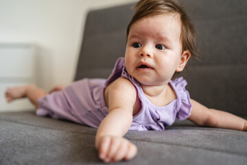 Fototapeta premium Close up portrait of small caucasian baby girl four months old lying on the bed couch sofa at home in summer day looking to the side copy space