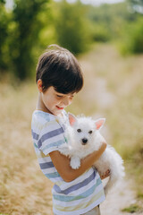Friendship of a child with a dog. Happy boy holding a West Highland White Terrier puppy in his arms.