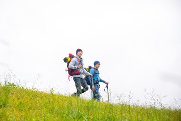  Two handsome Asian people man friends with backpack hiking together on mountain trail. Healthy male friendship enjoy outdoor activity and active lifestyle climbing and camping in summer vacation.