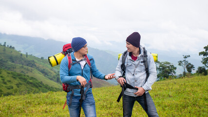  Two handsome Asian people man friends with backpack hiking together on mountain trail. Healthy male friendship enjoy outdoor activity and active lifestyle climbing and camping in summer vacation.