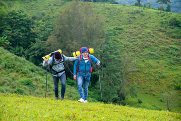  Two handsome Asian people man friends with backpack hiking together on mountain trail. Healthy male friendship enjoy outdoor activity and active lifestyle climbing and camping in summer vacation.