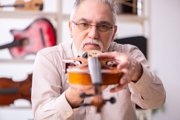 Old male repairman repairing musical instruments at workplace