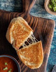 Top down view of a homemade grilled cheese sandwich on a wooden board, served with tomato soup.