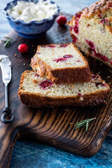Close up of a sliced cranberry rosemary quick bread with cream cheese topping in behind. 