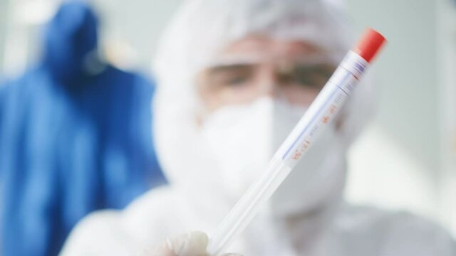 PCR test in laboratory, doctor looking at COVID-19 swab collection kit, lab worker wearing PPE medical suit, mask, gloves, holding test tube for taking OP NP specimen. Express coronavirus analysis 