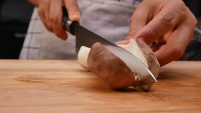 Close-up of female hands slicing oringi mushrooms or royal oyster mushroom using a knife on the cutting board. Concept of preparing healthy meal.