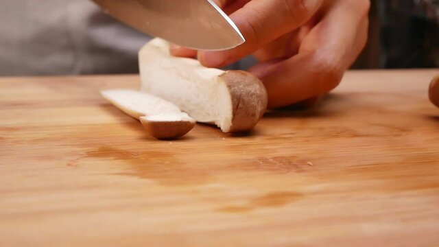 Close-up of female hands slicing oringi mushrooms or royal oyster mushroom using a knife on the cutting board. Concept of preparing healthy meal.