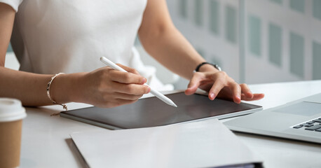 Young business woman hands holding pen stylus and working on black digital tablet pc with laptop...