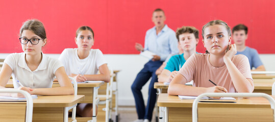 Teenage students are sitting at their desks in classroom. In background the teacher. High quality photo