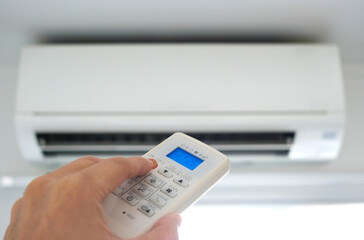 Man's hand using remote control open The air conditioner is cooled to 25 degrees Celsius in his bedroom. Health concepts and energy savings