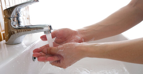 Hands of woman wash their hands in a sink with foam to wash the skin and water flows through the hands. Concept of health, cleaning and preventing germs and coronavirus from contacting hands