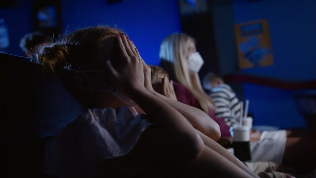 Worried small children covering eyes in the cinema while watching film.
