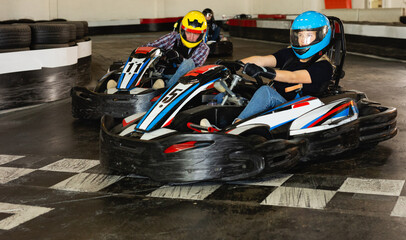 Young man and women competing on racing cars at kart circuit - obrazy, fototapety, plakaty