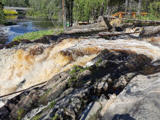 The picturesque Ahvenkoski waterfall on the Tokhmayoki River in Karelia with a suspension bridge over it on a clear summer morning.