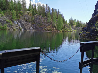 A view from a floating platform on the side of a flooded Marble Canyon, where trees grow, in the Ruskeala Mountain Park on a sunny summer day.