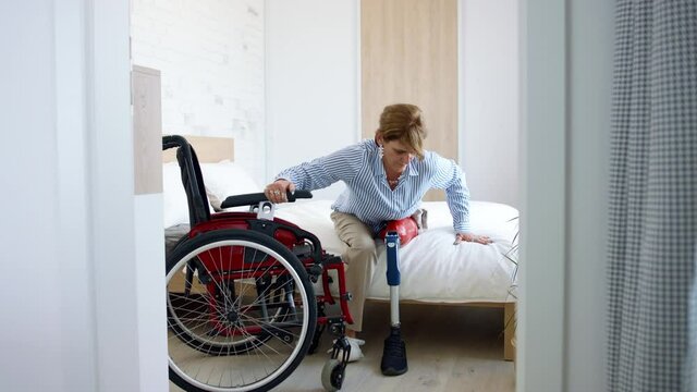 Disabled mature woman getting up from bed indoors at home, leg prosthetic concept.