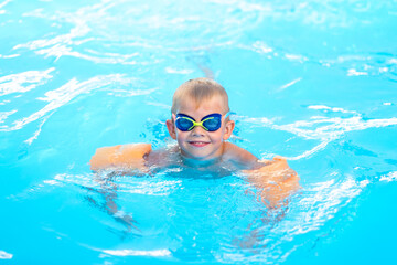 Naklejka premium Portrait smiling boy in swimming pool, child in swimming glasses and inflatable sleeves. Summer travel hotel vacation or classes