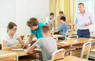 Fototapeta premium Concentrated teen girls and boys discussing in small groups, trying to solve teacher assignments together. Active learning concept