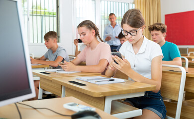 Teenager students sitting in class room and using their smartphones.