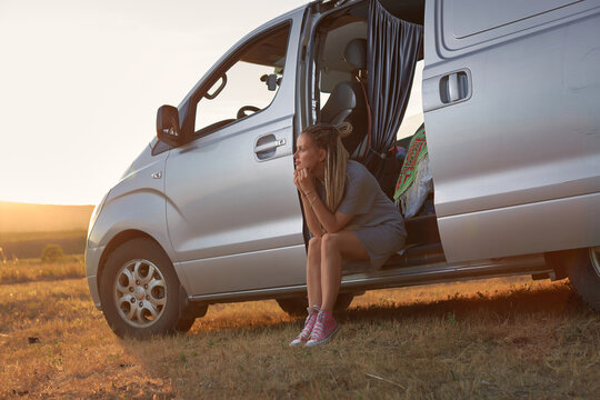 a hippie girl sits in her minivan with the door open against the background of the outgoing sun. The concept of youth and freedom. High quality photo