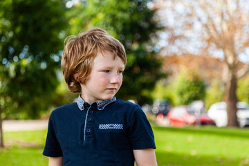 profile of unsure young autistic boy looking to the side at a park outside