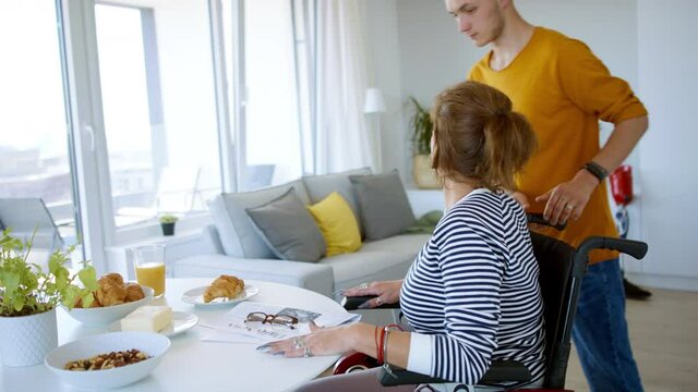Disabled mature woman in wheelchair having a breakfast with her son.
