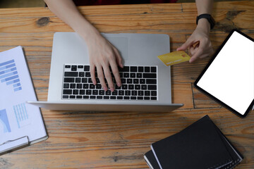 Female holding credit card and using computer laptop on wooden desk.