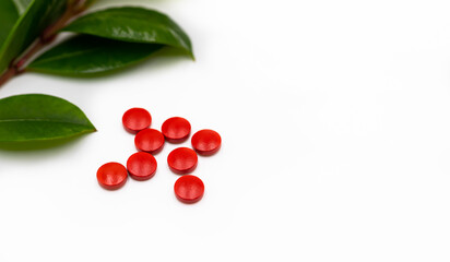 Red pills with leaves from fresh green source herbs in a display isolated on a white background.	