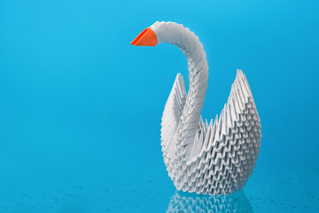 White origami swan made of paper with a red beak on a blue background