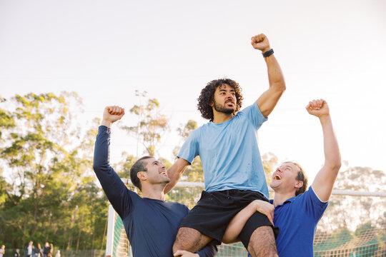 horizontal shot of two men carrying a man on their shoulders while raising their arms up high