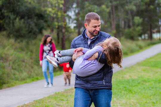 Family walking together through park focus on father carrying child
