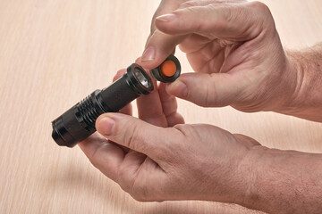 Hands hold a small black flashlight and replace the battery in it