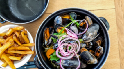 A pot of freshly cooked  mussels garnished with purple onion and roasted potato chips, french fries, a traditional Belgian dish. Close up, top view.