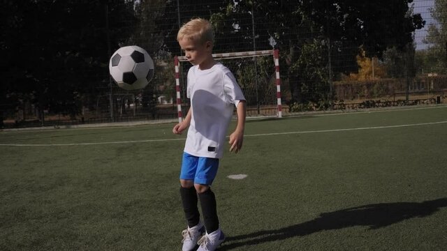 A little boy soccer player learns to juggle the ball on the football field.