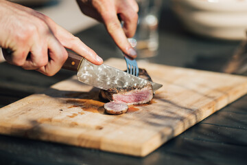 Cutting medium rare grilled tenderloin steak on a wooden board
