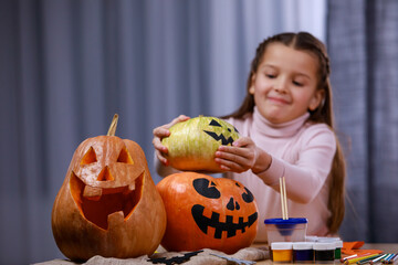 Preparing for Halloween. On the table are pumpkins with a painted and carved terrible face, the girl lays down another one. Halloween. Close up.