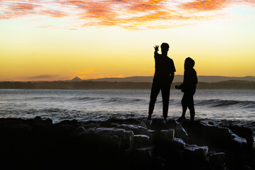 Silhouette of Two Friends Standing on Rocks Close to Ocean at Sunset in Noosa,Queensland,Australia