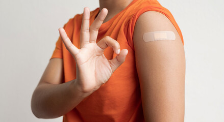 Asian woman shows plaster on her shoulder after being vaccinated against Covid-19. Coronavirus vaccination campaign concept