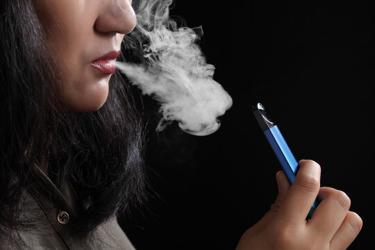 Close up young woman smoking e-cigarette on black background