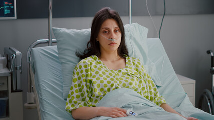 Patient wearing with nasal oxygen tube looking into camera sitting in bed recovering after...