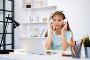 Naklejka premium Little caucasian girl in headphones have video call distant class with teacher at home