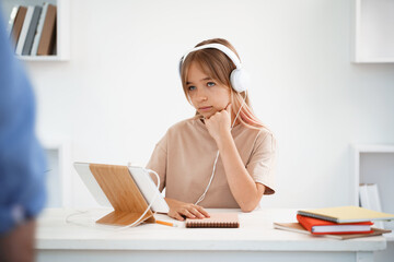 Little caucasian girl in headphones have video call distant class with teacher at home