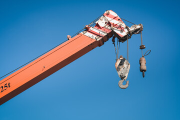 Boom Lifting Crane With Cable Hook Against Blue Sky Background. Hydraulic Lifting Mover of Mobile Machine During Operation in Construction Site. Lifter Machinery Component for Moving Heavy Objects