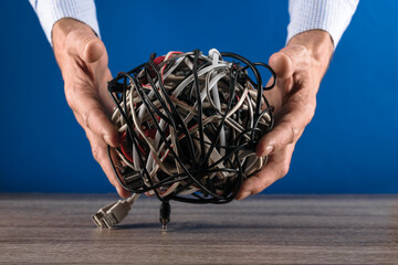 Closeup of male hands showing bunch of tangled wires against blue background