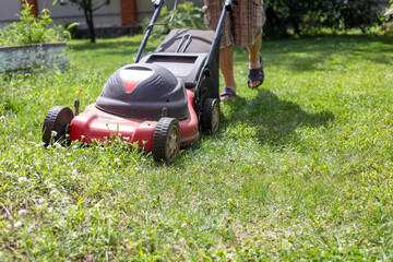 mowing grass with a lawnmower in hard-to-reach places on a sunny warm day, horizontal.