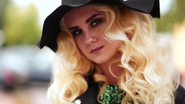 Stylish blonde girl in a black hat and curly hair looks at the camera and smile. Video